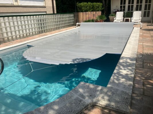 Grijze Liderpool foam cover die gedeeltelijk is uitgerold over een rechthoekig zwembad, gemonteerd op een oprolas voor isolatie en bescherming tegen vuil.